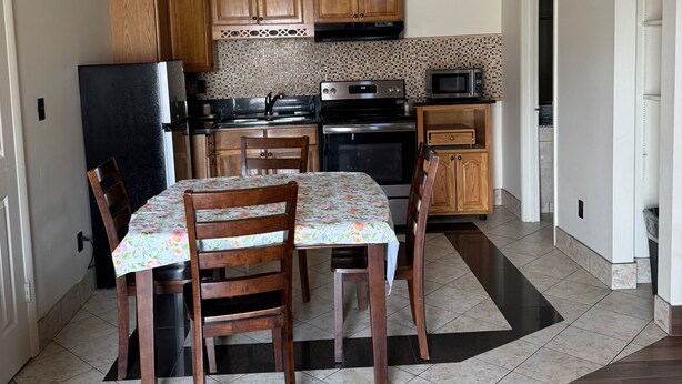 A kitchen with wooden cabinets, a refrigerator, stove, microwave, and a dining table with chairs. - Snowbird Motel (Bristol)