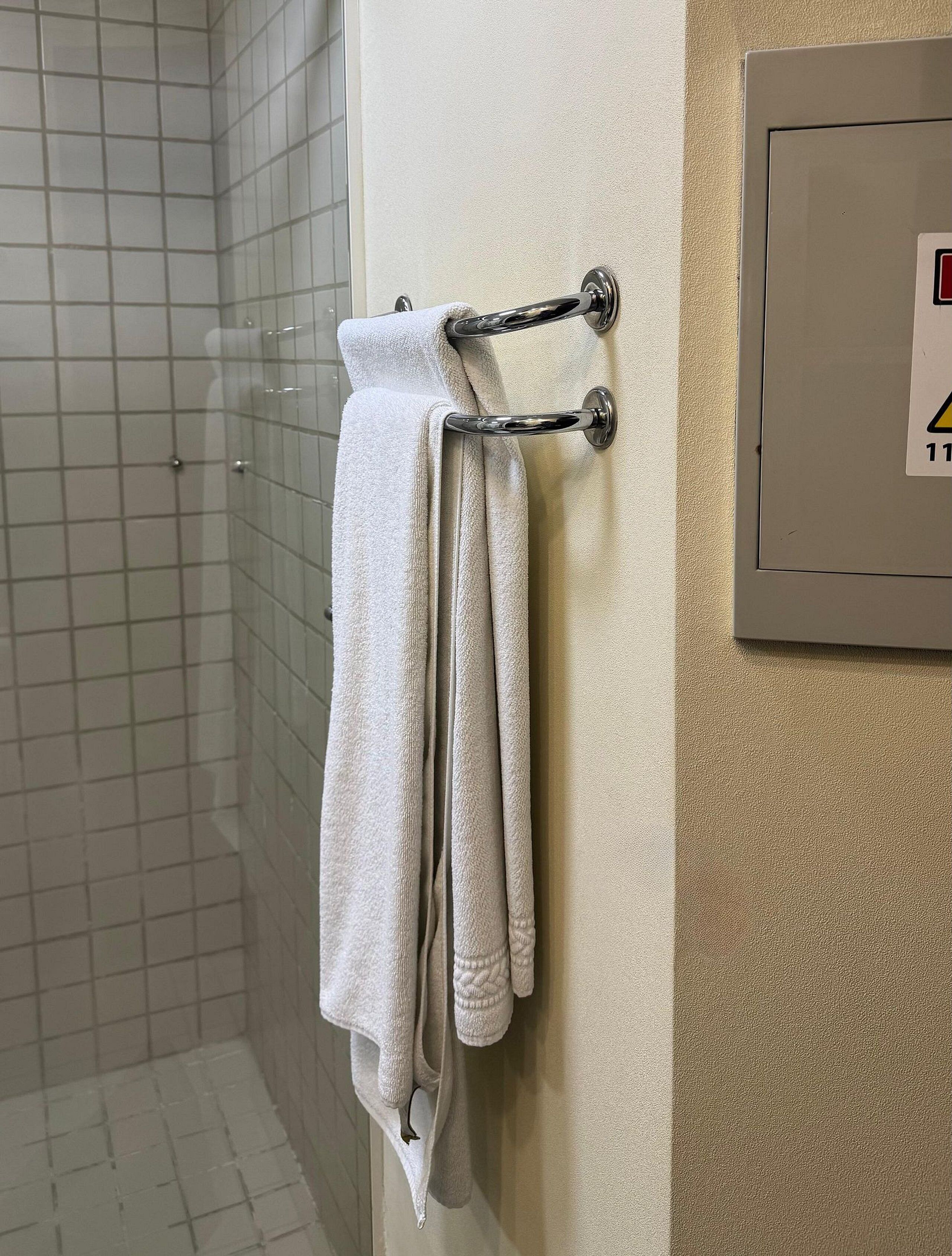 A bathroom with a towel rack holding two towels, a tiled shower area, and a wall-mounted electrical panel.