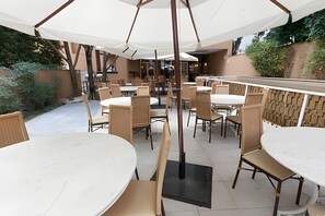An outdoor patio area with round tables and chairs, covered by white umbrellas, and surrounded by a stone wall. - Get a Flat 100mts Av. Paulista - Jardins (São Paulo)