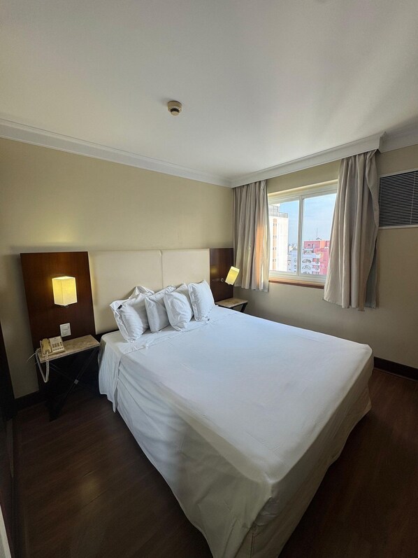 A hotel room with a large bed, bedside lamps, a telephone, and a window with curtains. - Get a Flat 100mts Av. Paulista - Jardins (São Paulo)