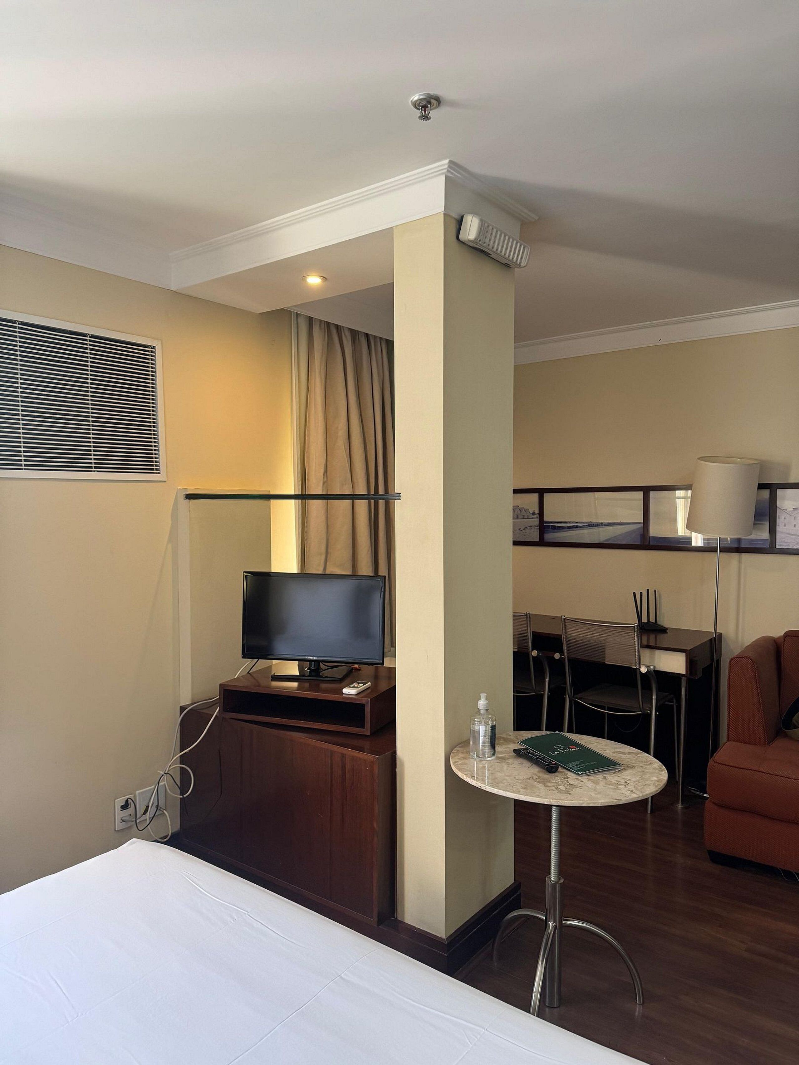 Ein Hotelzimmer mit Bett, Fernseher, einem kleinen Tisch mit Fernbedienung, einem Sessel und einer Couch.