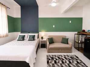 Une chambre à coucher comprenant un lit, un canapé, une table de chevet, une lampe et un tapis à motifs géométriques.