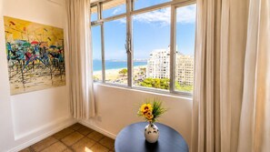 A room with a large window, a painting on the wall, and a vase with flowers on a table. - Amazing sea view in Copacabana (Rio de Janeiro)