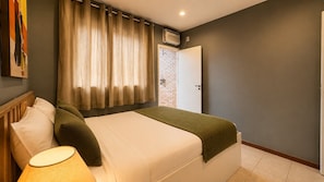 A hotel room with a bed, a bedside lamp, a window with curtains, and a door leading to a brick wall.