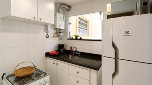 Een moderne keuken met witte kastjes, een zwarte aanrechtblad, een fornuis, een koelkast en een raam met jaloezieën.