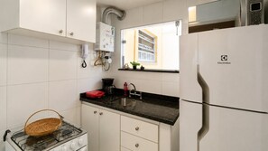 Eine moderne Küche mit weißen Schränken, einer schwarzen Arbeitsplatte, einem Herd, einem Kühlschrank und einem Fenster mit Jalousien.