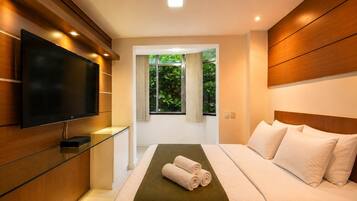 Quarto de hotel moderno com televisão de tela plana, cristaleira, cama com lençóis brancos e vista para o verde pela janela.