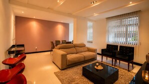 A modern living room with a beige sofa, a coffee table, and red chairs. - Confortável 3Qts: Vista Lateral Mar (Rio de Janeiro)