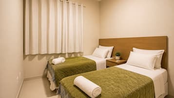 A hotel room with two beds, a wooden headboard, a nightstand, a potted plant, and a window with curtains.