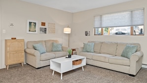 A living room with two beige sofas, a white coffee table, a wooden cabinet, and a floor lamp. - Chic Central Nook in Great Falls (Great Falls)