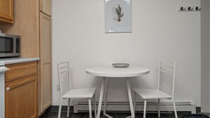 A small, white dining area with two chairs and a table, a microwave, and wooden cabinets. - Chic Central Nook in Great Falls (Great Falls)