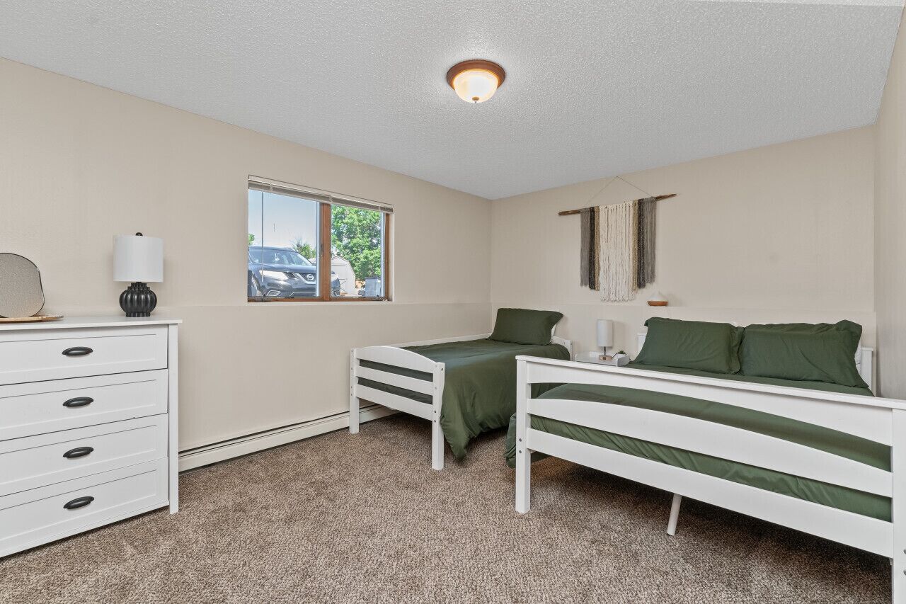 A bedroom with two single beds, a dresser, a window, and a ceiling light.
