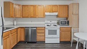A kitchen with wooden cabinets, a stainless steel dishwasher, a white stove, and a microwave. - Chic Central Nook in Great Falls (Great Falls)