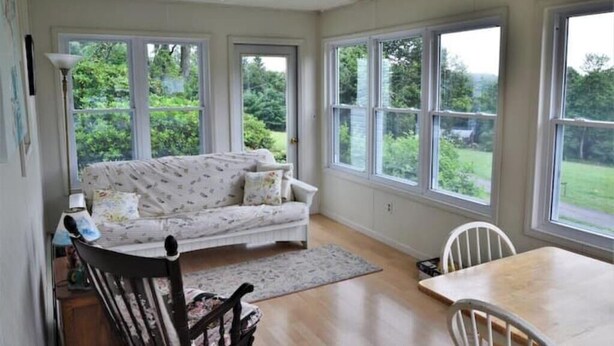 A cozy room with a sofa, a dining table, and chairs. Large windows offer a view of greenery outside. - Five W Ranch -Sugar Hill Farm location- Private, Five Minutes From Downtown!

 (Saint Marys)