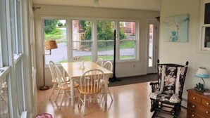 A dining area with a table and chairs, a chair with a floral pattern, and a view of a green landscape through large windows. - Five W Ranch -Sugar Hill Farm location- Private, Five Minutes From Downtown!

 (Saint Marys)
