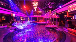 Un espace piscine intérieur luxueux, doté d’une fontaine centrale, entouré de sièges et illuminé par un éclairage dynamique.
