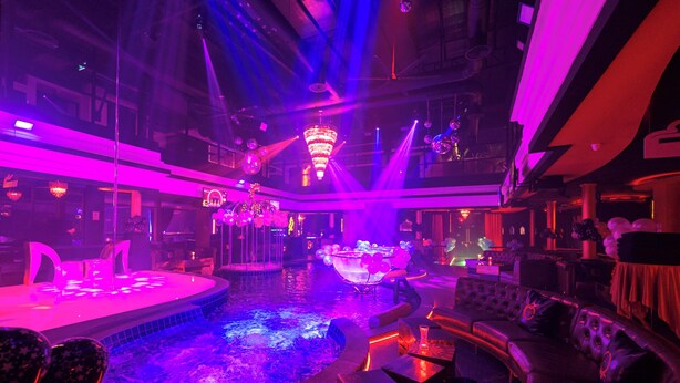 Un espace piscine intérieur luxueux, doté d’une fontaine centrale, entouré de sièges et éclairé d’une lumière d’ambiance.
