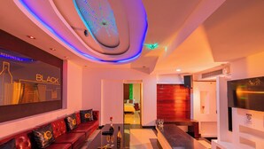 Une chambre d’hôtel moderne avec un canapé en cuir rouge, une table basse noire et une fresque murale représentant un paysage urbain.
