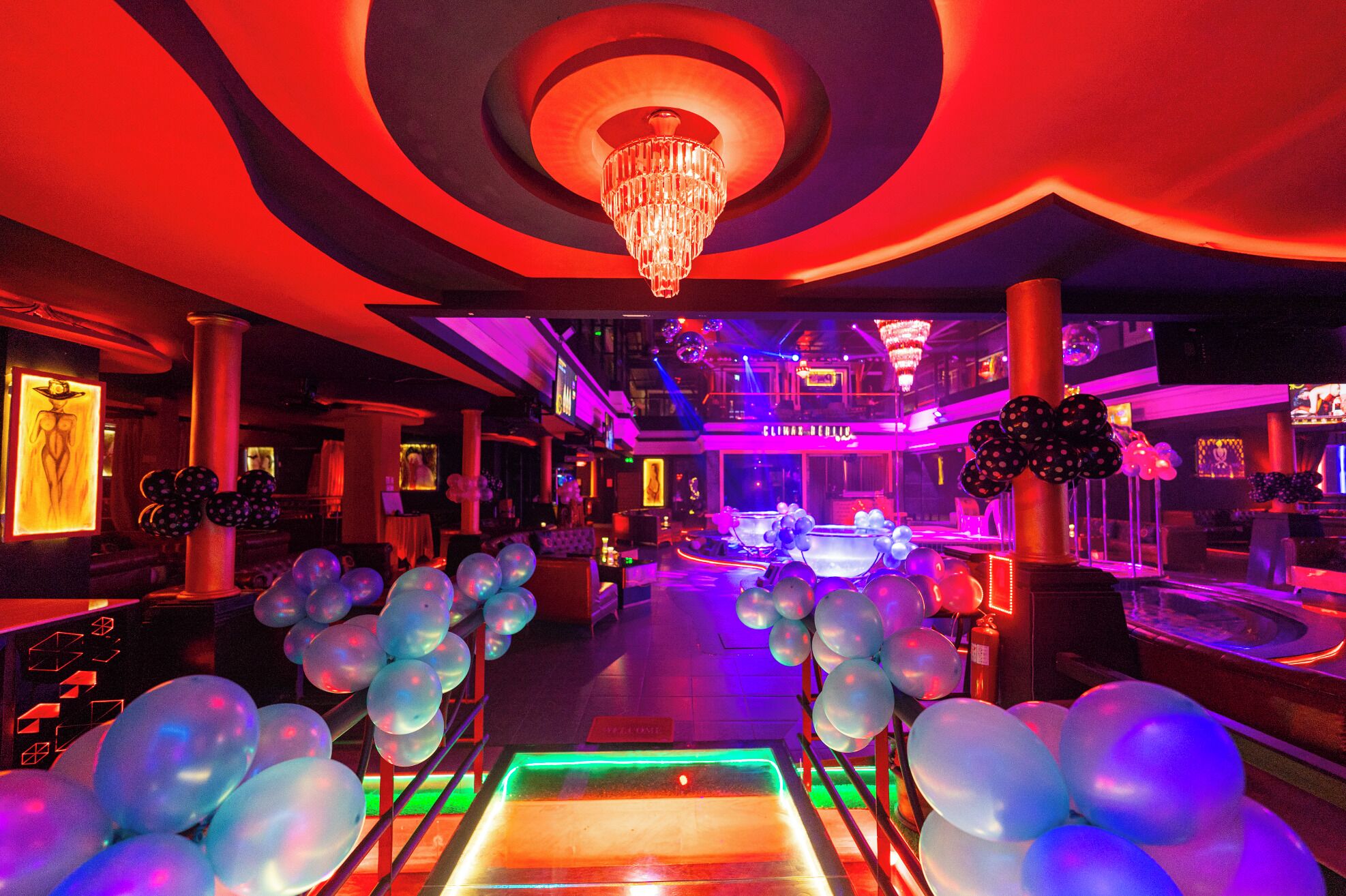 A brightly lit corridor with a chandelier, balloons, and neon lights.