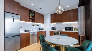 Une cuisine moderne avec des meubles en bois, des appareils en acier inoxydable et une table ronde en marbre, entourée de chaises vertes.