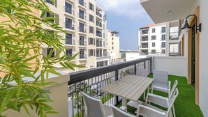 Un balcon agrémenté d’une table et de chaises, entouré de verdure et offrant une vue sur un quartier résidentiel composé de plusieurs immeubles.
