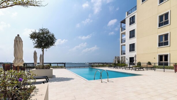 Une piscine sur le toit, offrant une vue sur la mer, entourée d’un bâtiment doté de balcons et d’un espace extérieur aménagé pour s’asseoir.