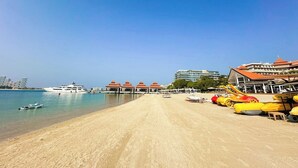 Ein Strand mit einer vor Anker liegenden Yacht, einem Rettungsschwimmturm und einem Gebäude mit rotem Dach.