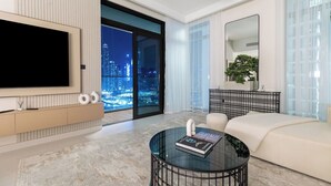 A modern living room with a large TV, a glass coffee table with a book, a sofa, and a city view through large windows.