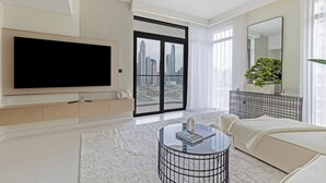 A modern living room with a large flat-screen TV, a glass coffee table, a sofa, and a view of a cityscape through a large sliding door.