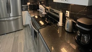 A modern kitchen with stainless steel appliances, a black countertop, and white cabinets.