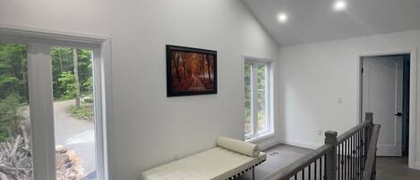 Een ruime kamer met een hoge plafond, grote ramen en een houten trap met een leuning.