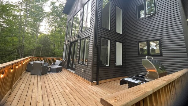 A modern two-story house with a deck, large windows, and outdoor seating.