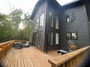 Een modern huis met twee verdiepingen, een terras, grote ramen en buiten zitplaatsen.