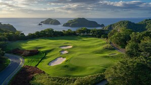 Ein Golfplatz mit Bunkern, einer Straße und Blick auf das Meer und Inseln.