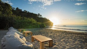 Ein Strand mit einer Holzbank und einem Tisch, umgeben von Sand und Pflanzen.