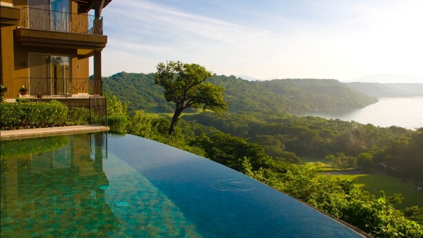 A hotel with a pool overlooking a mountainous landscape and a body of water.