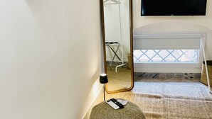 A hotel room with a large mirror, a flat-screen TV, a bed with a white headboard, a window with a view, and a small table with a lamp and remote control. - Capo - Single Room (Butera Apartments Luxury) (Palermo)