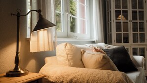 Et hyggeligt værelse med en lampe på et trænatbord, en polstret bænk med puder, og et vindue med gardiner.