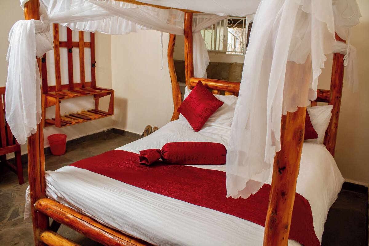Una cama con dosel de madera, ropa de cama y almohada rojas.
