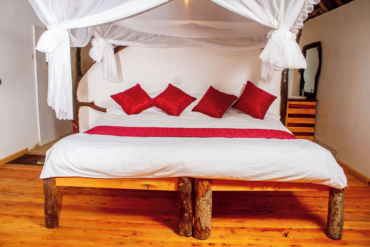 Una cama con dosel blanco y almohadas rojas, patas de madera y colcha roja.
