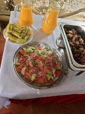 Una mesa con una ensalada, frutas cortadas y un plato de carne, junto con dos jarras de jugo de naranja.