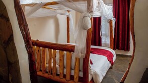 A rustic wooden bed with a canopy, a red curtain, and a stone floor. - Hillstone Safari Lodge (Kimana)