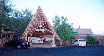 Un lodge de safari con estructura de techo triangular, una zona de recepción y un muro de piedra.