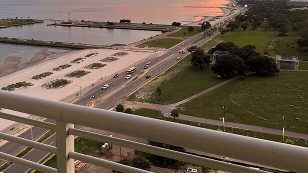 Eine Küstenstadtlandschaft bei Sonnenuntergang über dem Wasser, eine Straße mit Fahrzeugen und eine Brücke.
