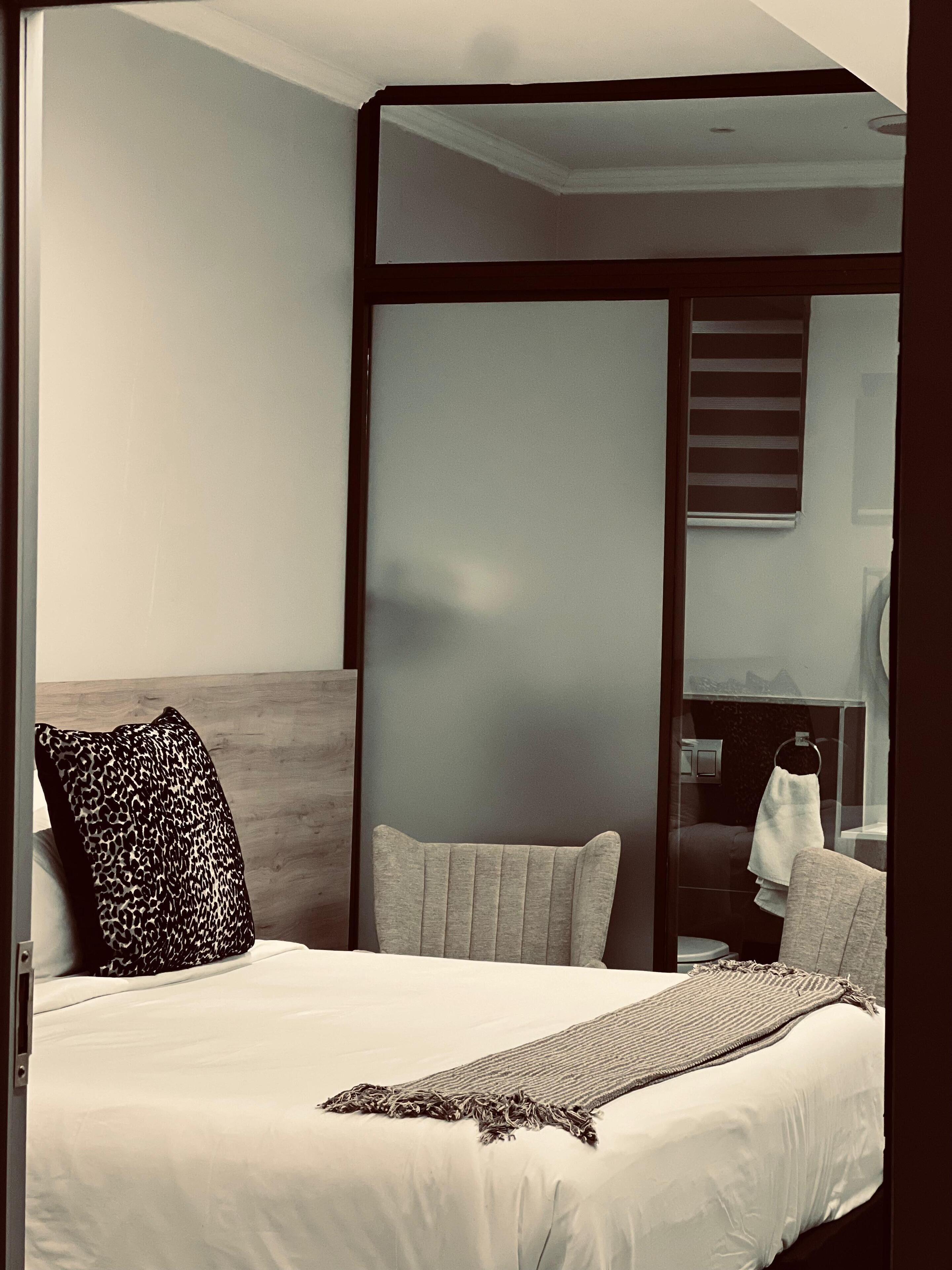 A modern hotel room with a large bed, a headboard, and a view of the bathroom through a frosted glass partition.
