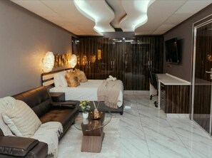 Ett modernt hotellrum med en soffa, en säng, ett skrivbord och en TV.