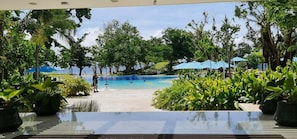A pool area with a view of the beach, surrounded by potted plants and umbrellas.