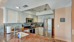 A kitchen with white cabinets, stainless steel appliances, a granite countertop, and a sign on the wall. - Gulfside Villas Unit 11... Steps to the Beach, Heated Pool Beautiful Townhome (Indian Rocks Beach)