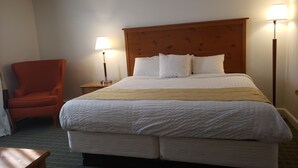A hotel room with a large bed, a wooden headboard, two bedside lamps, a red armchair, and a small wooden table. - Town & Country (Seekonk)