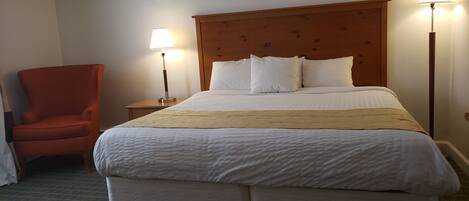 A hotel room with a large bed, a wooden headboard, two bedside lamps, a red armchair, and a small wooden table.